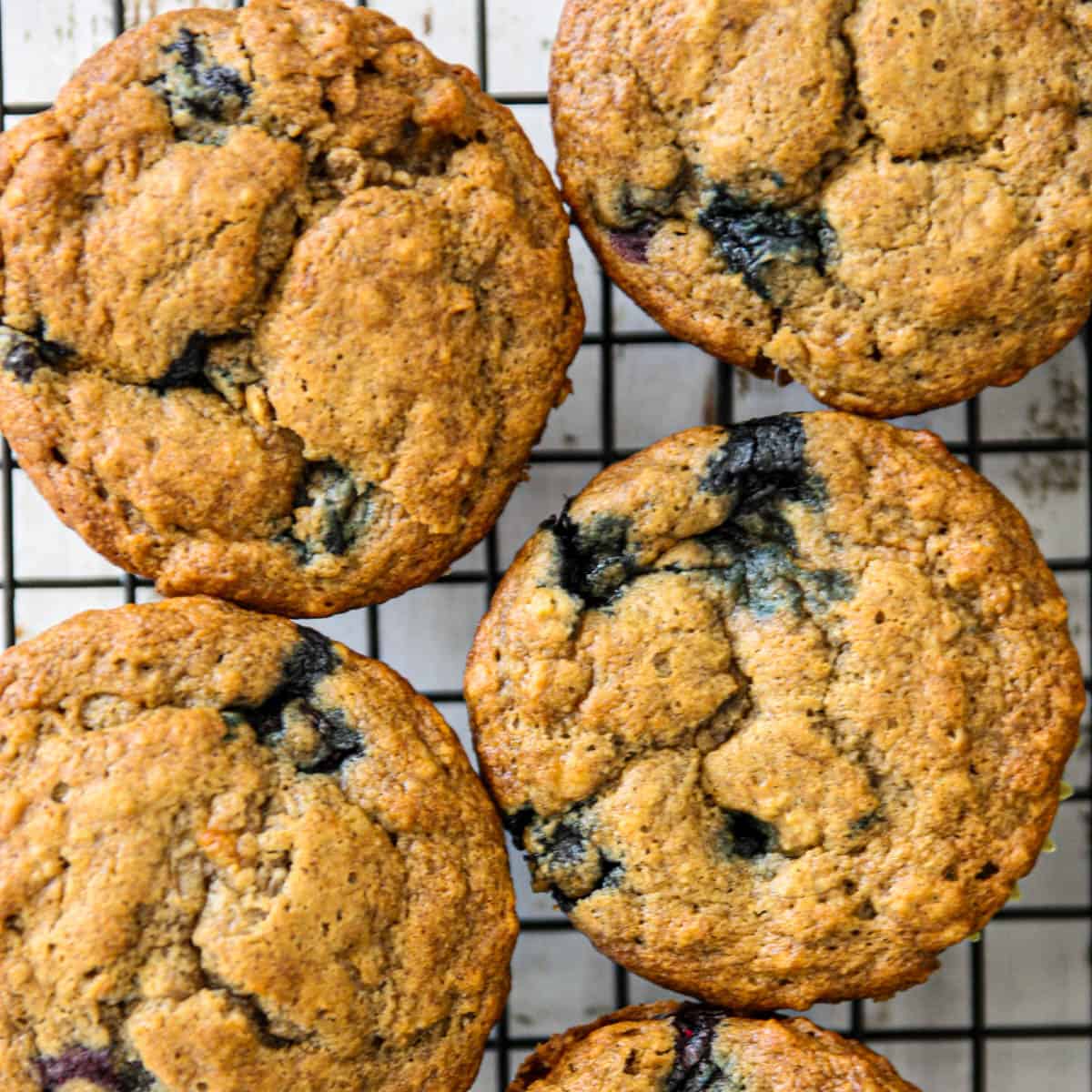 Four banana blueberry muffins on a wire rack.