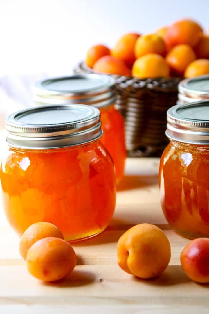 Four jars of apricot jam and a basket of fresh apricots