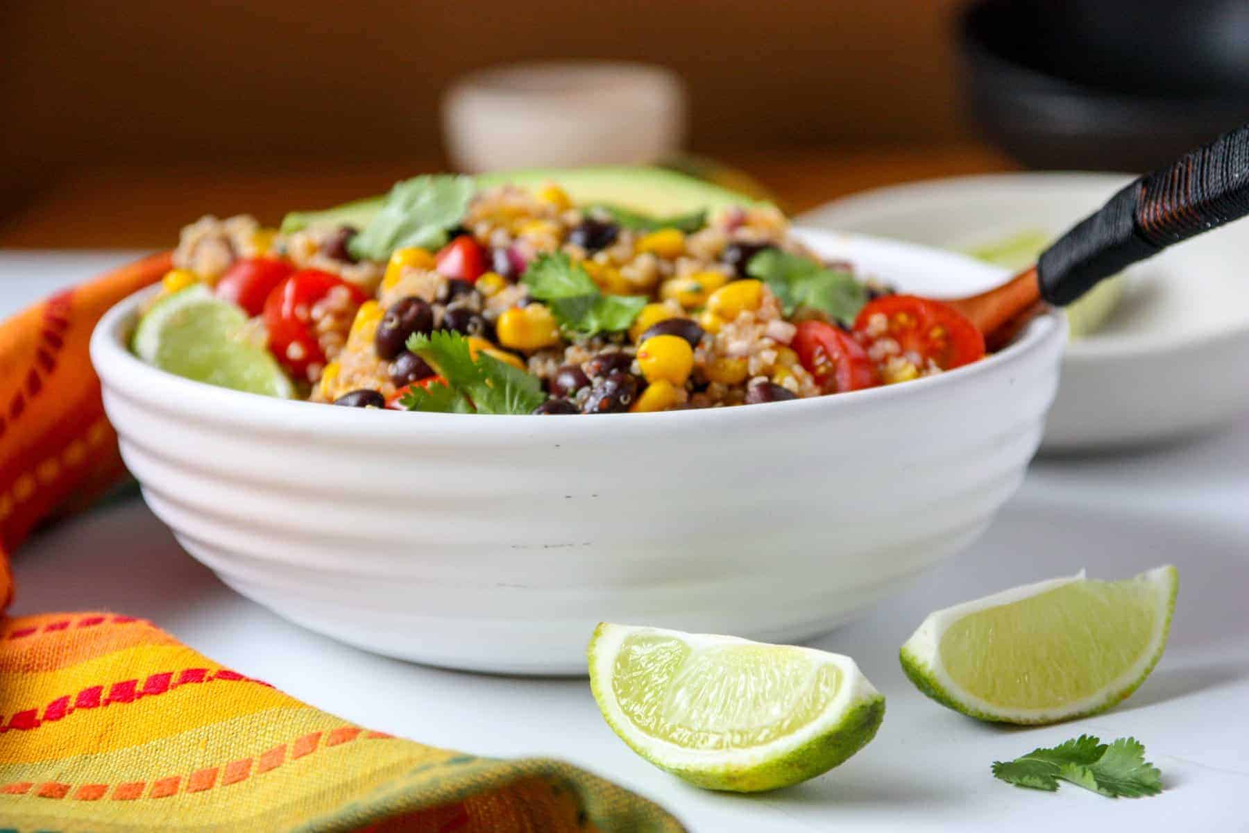 A white bowl filled with salad on a table, with lime wedges.