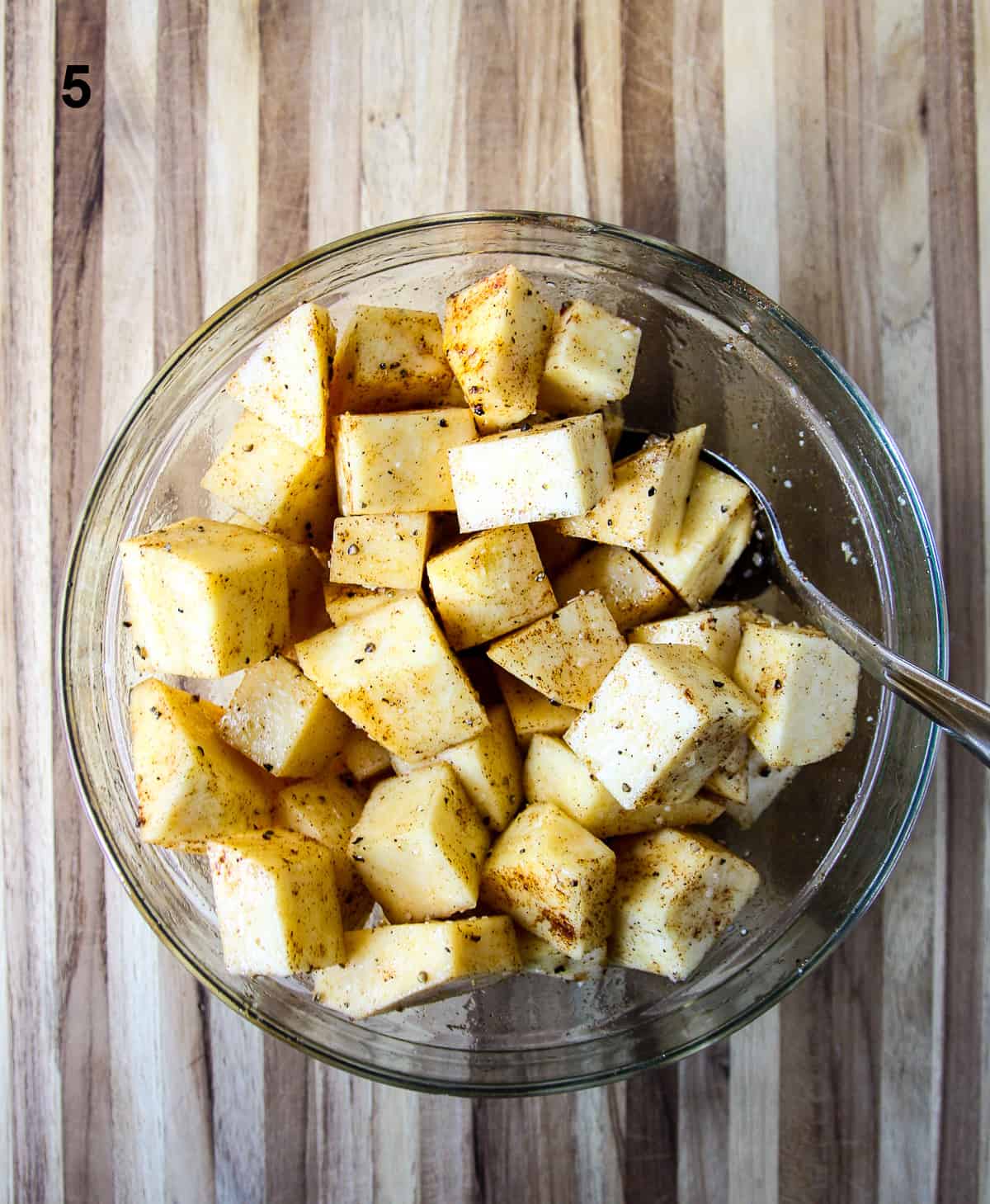 The cut cubes being tossed with seasoning and oil in a glass bowl.
