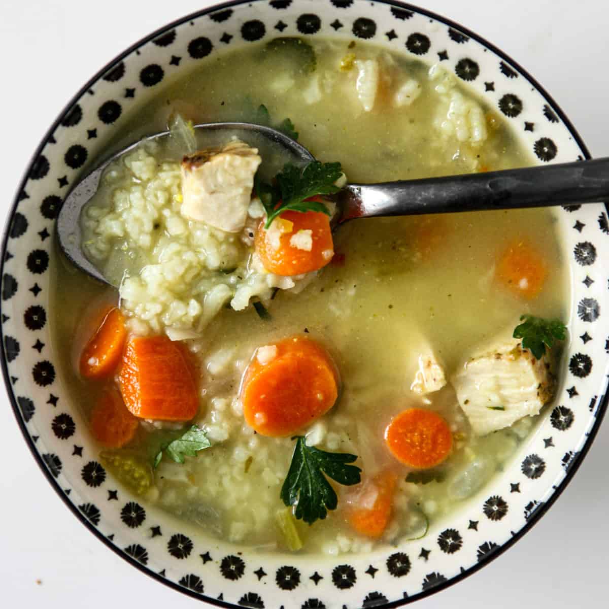 A spoon dipped into a bowl of turkey and rice soup.