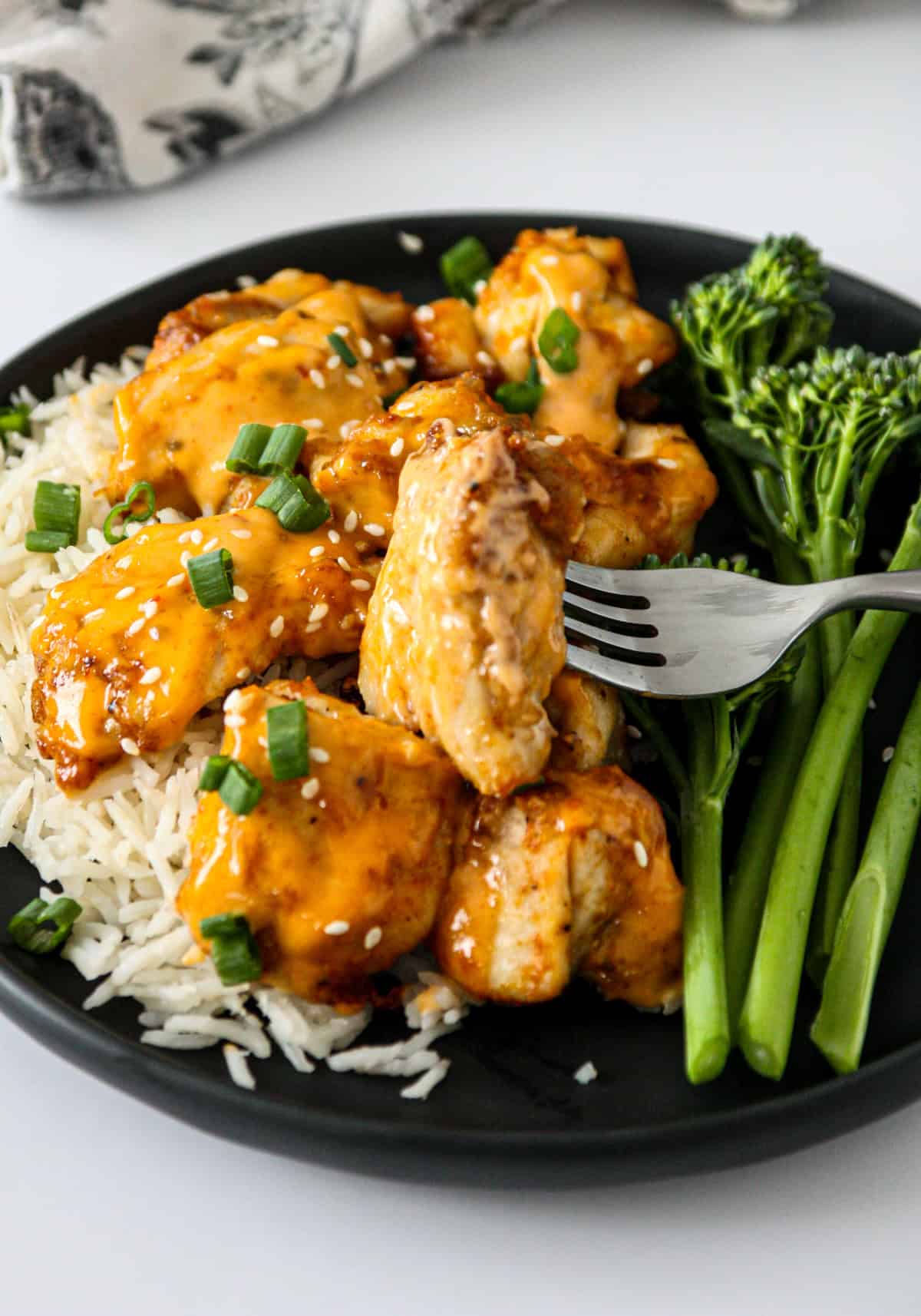 A fork holding a piece of bang bang chicken above a plate.