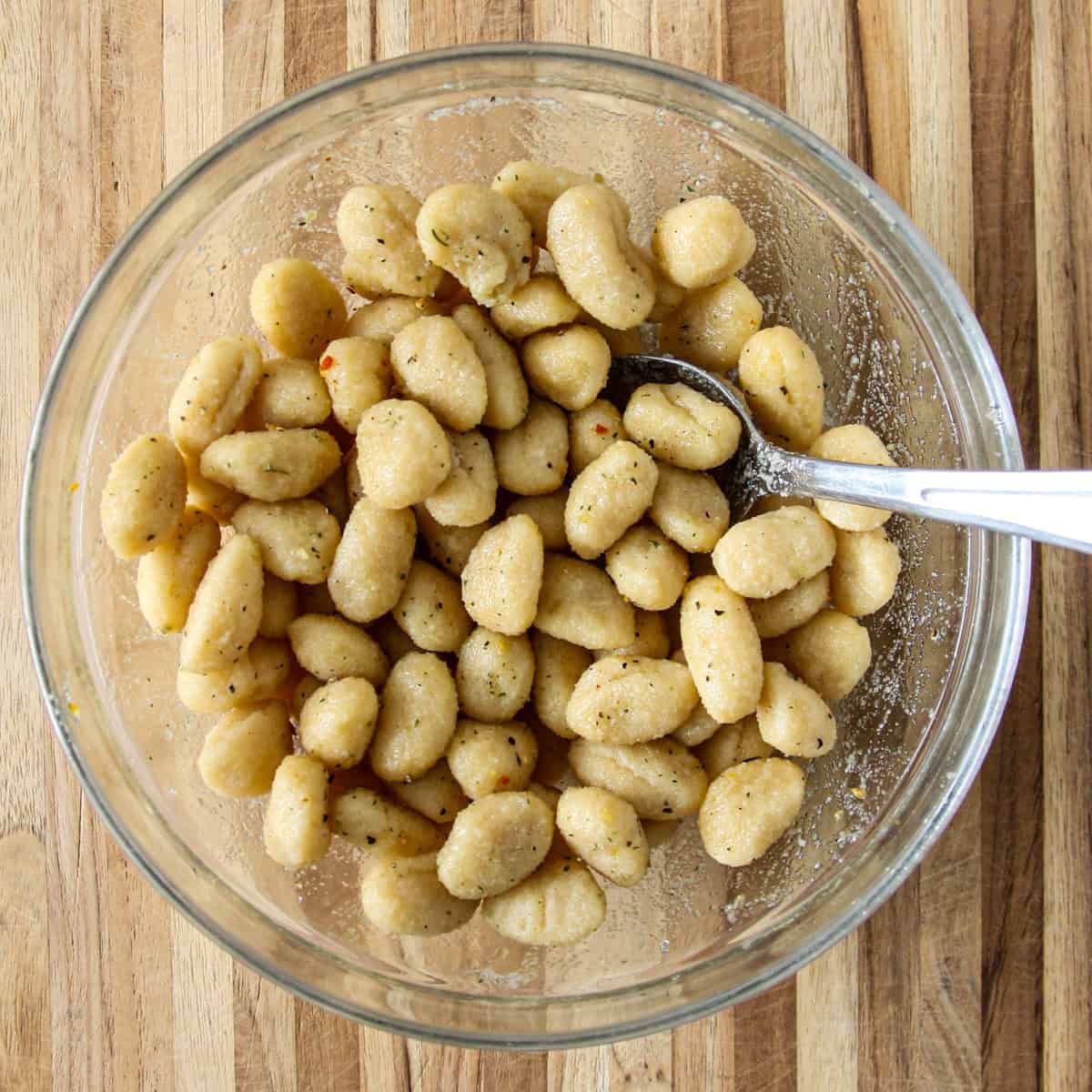 Uncooked gnocchi and seasonings stirred together in a mixing bowl.