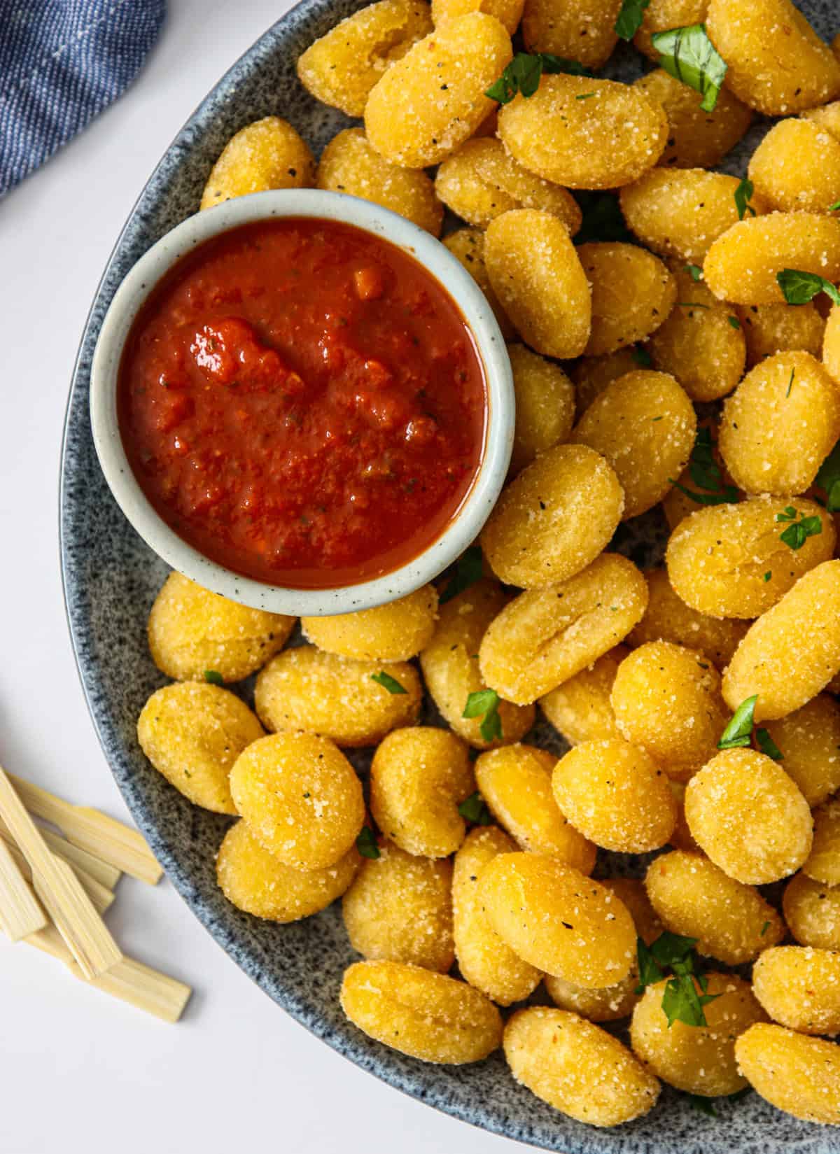 Air fryer gnocchi on a blue speckled plate with a small dish of marinara dip.